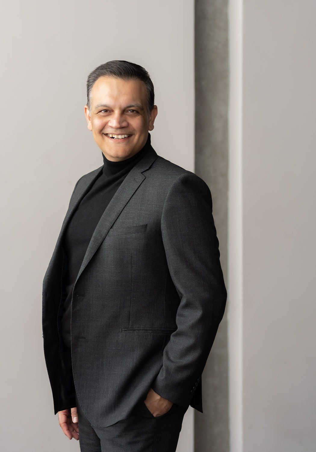 a man with a black turtle neck top and a black coat smiling at the camera