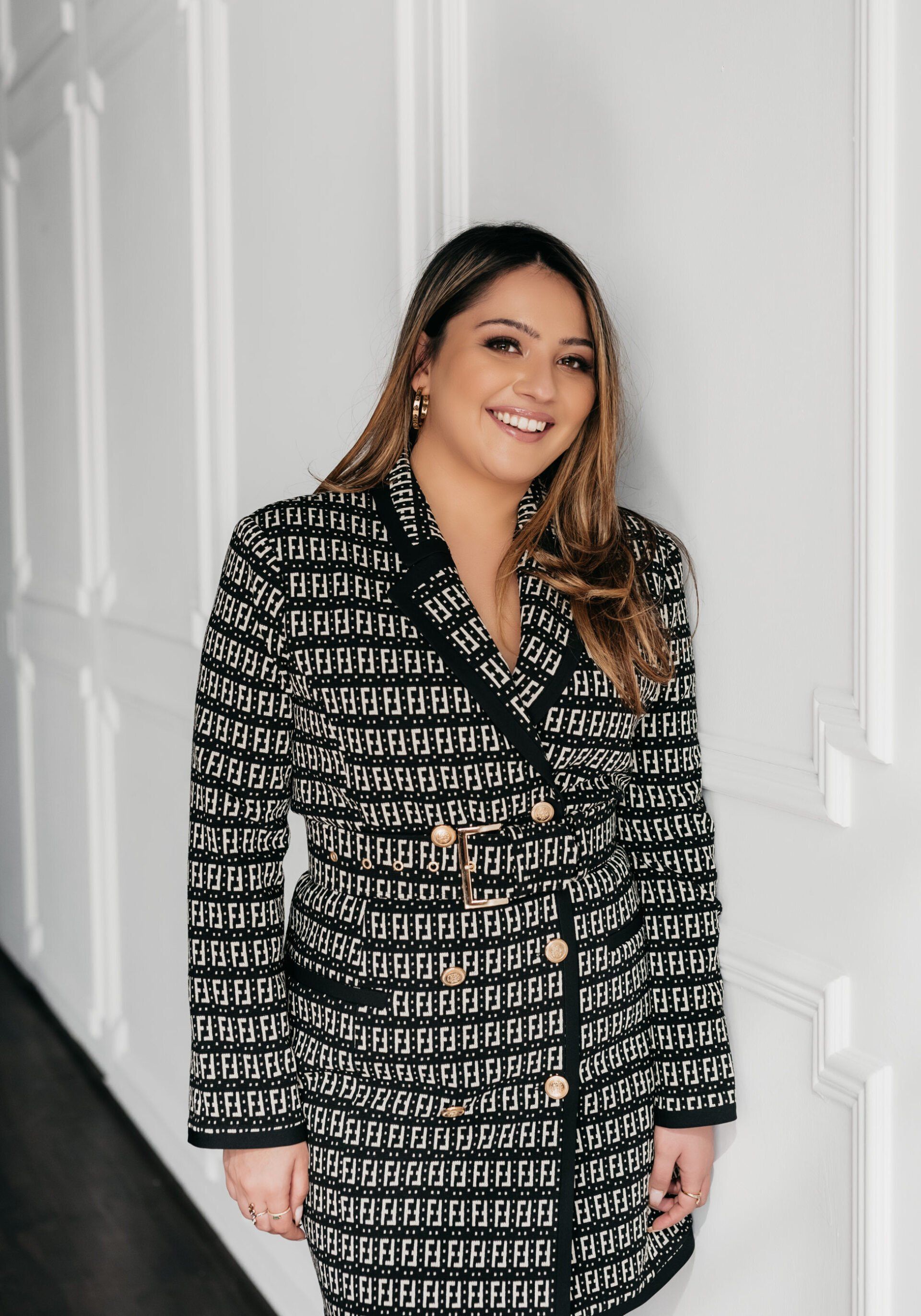 a woman wearing checkered coat dress smiling at the camera while leaning at the wall