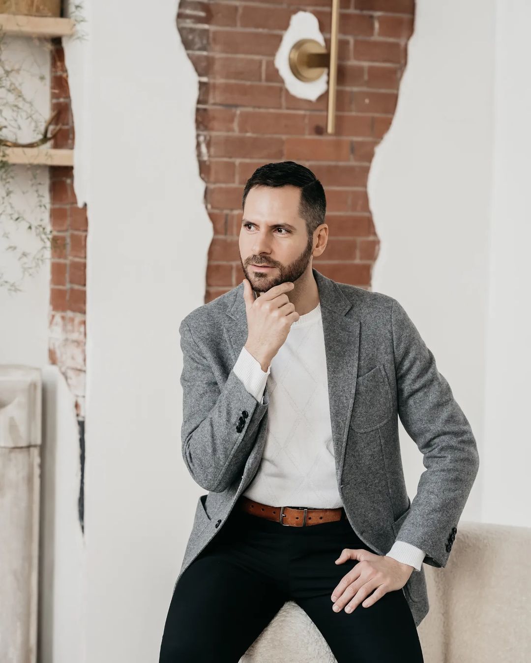 man wearing white t-shirt and gray suit holding his chin for a pose