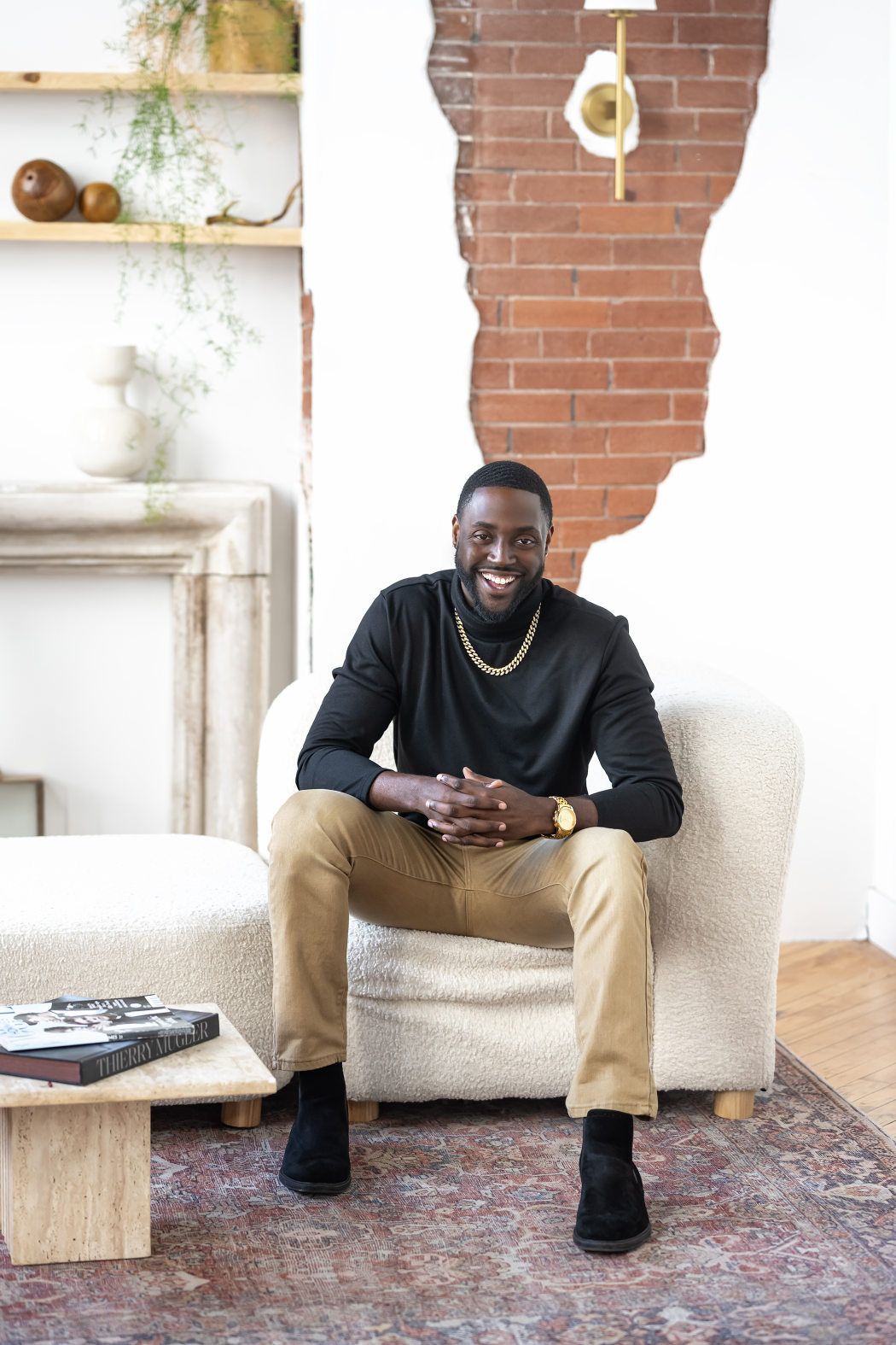 A man, seated on a white couch in a living room smiling at the headshot photographer