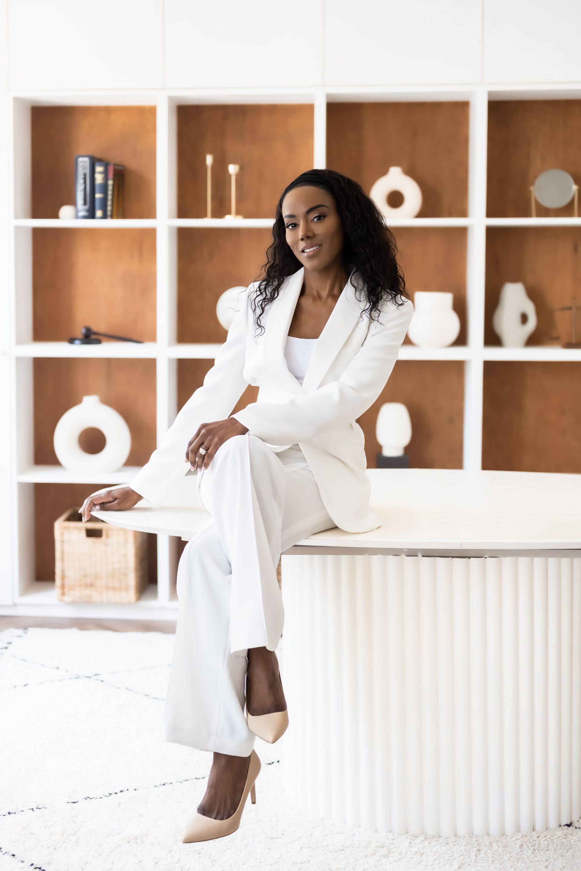 Professional personal branding photography of a woman in white attire, posed elegantly on a table, with decorative background elements.