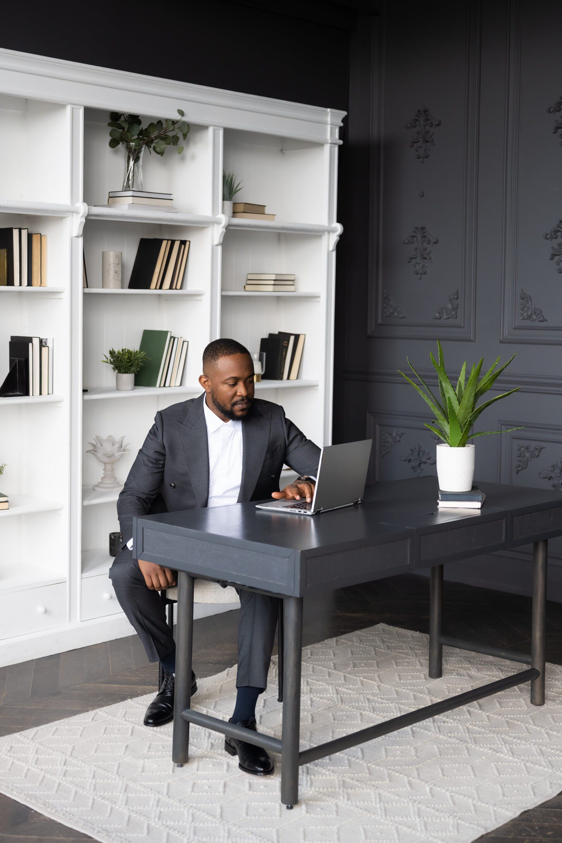 a man in a suit sitting at a desk in front of a bookcase.
