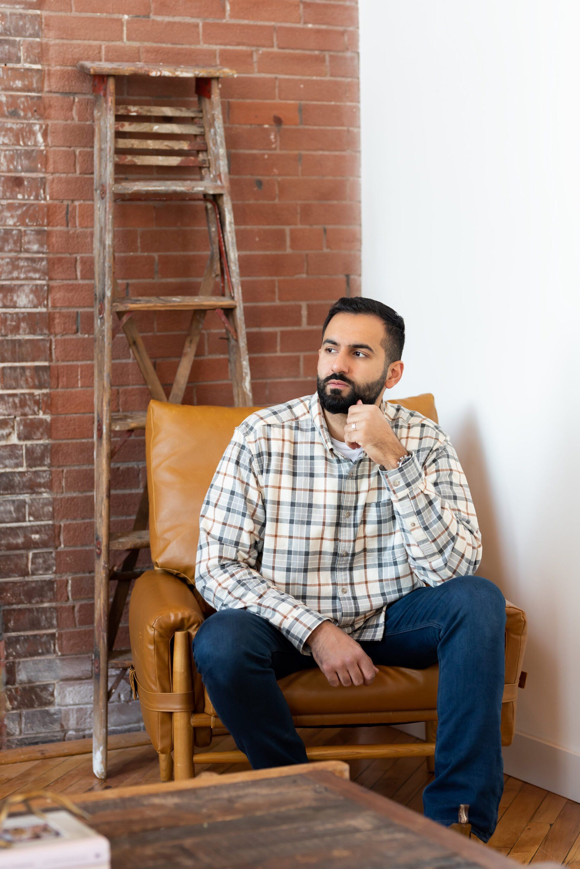 a man with a checkered top sitting in leather chair with a ladder in the background
