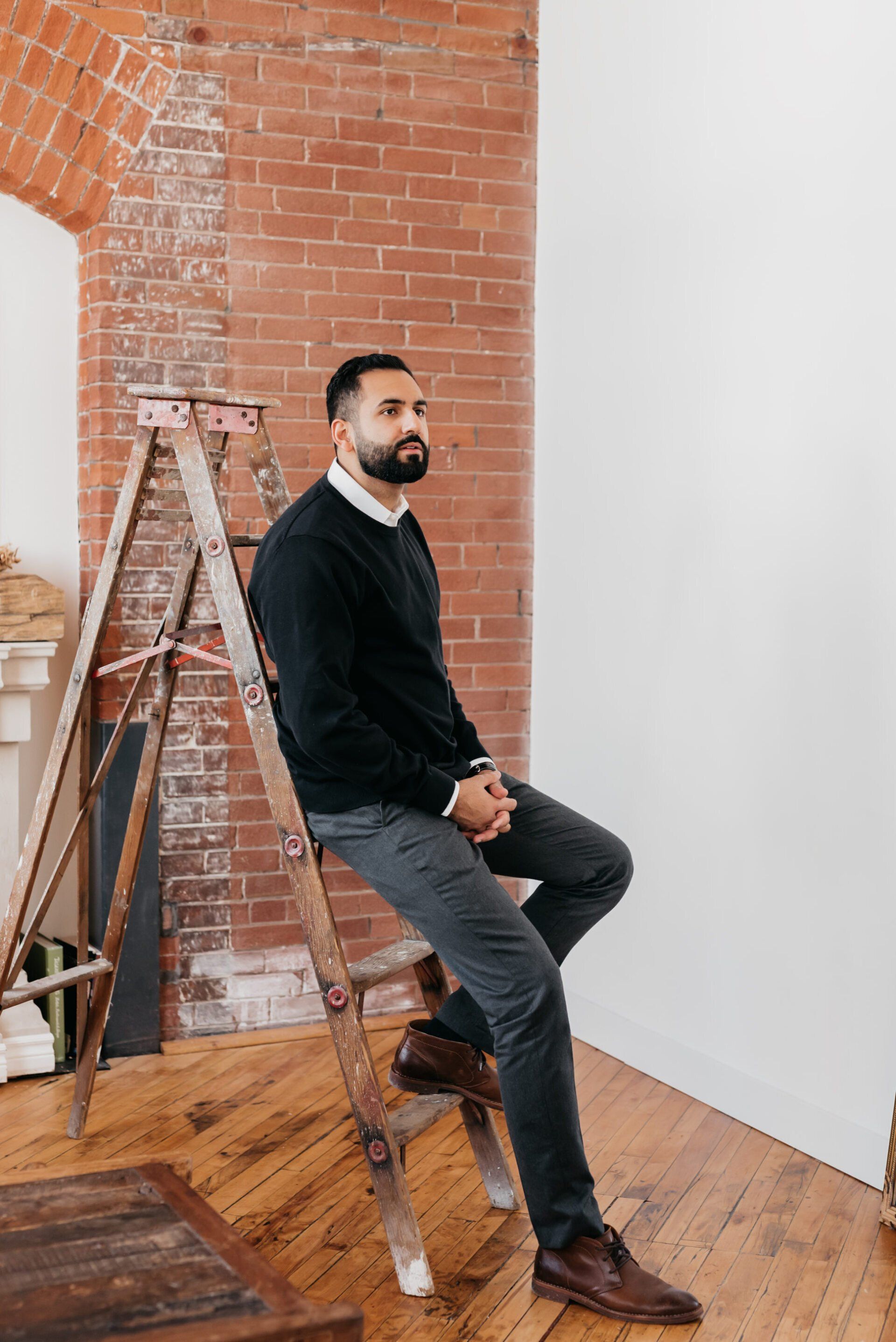 a man wearing a black top leaning against a ladder