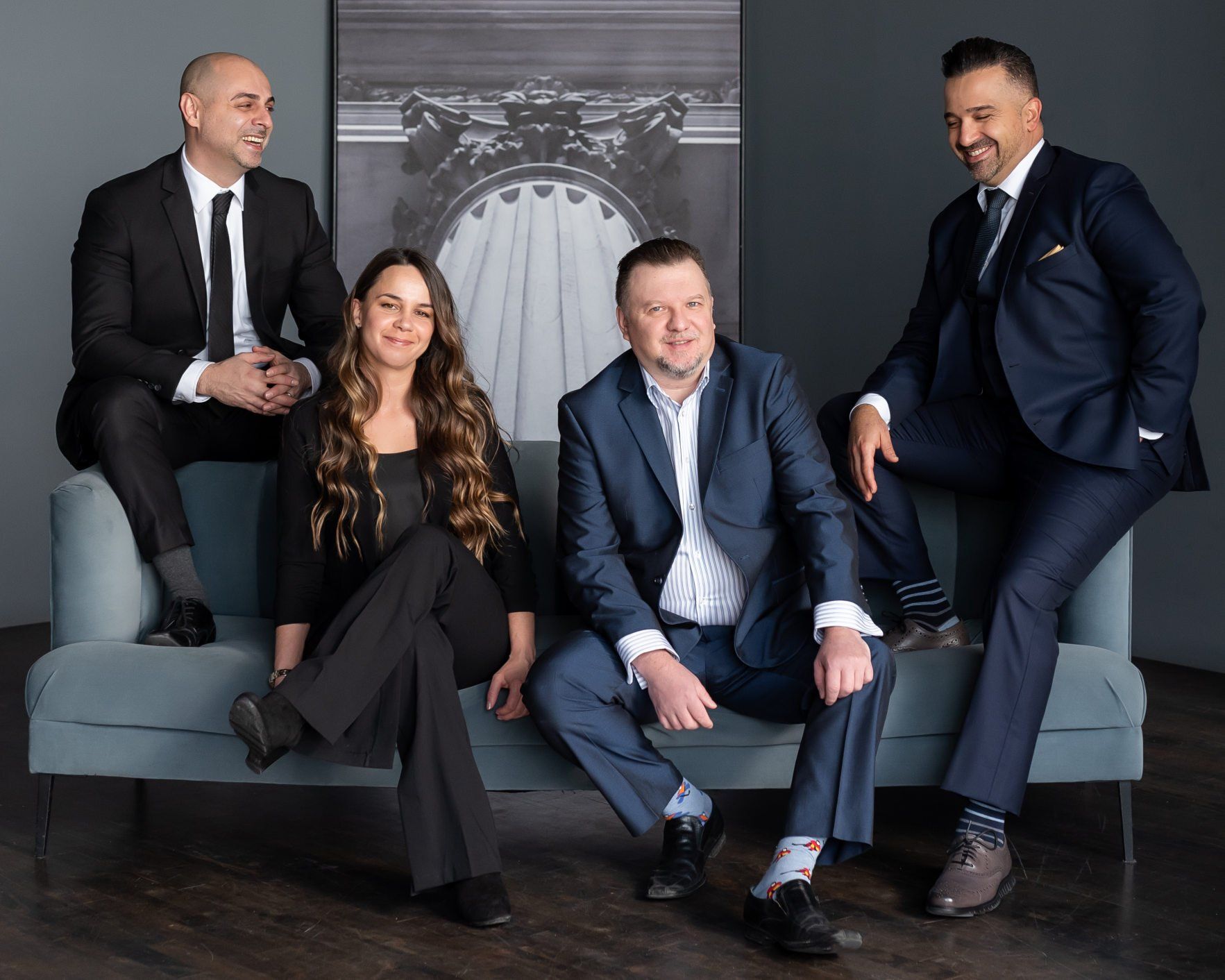 Four smartly dressed realtors smiling and sitting on a couch.