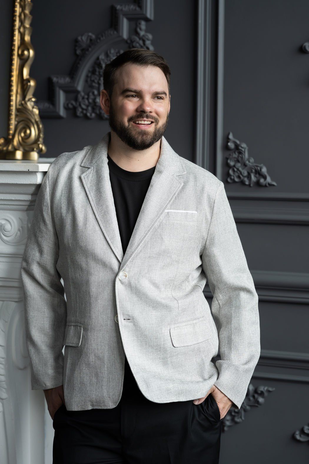 A Headshot of a man wearing a grey blazer with a victorian themed interior as background