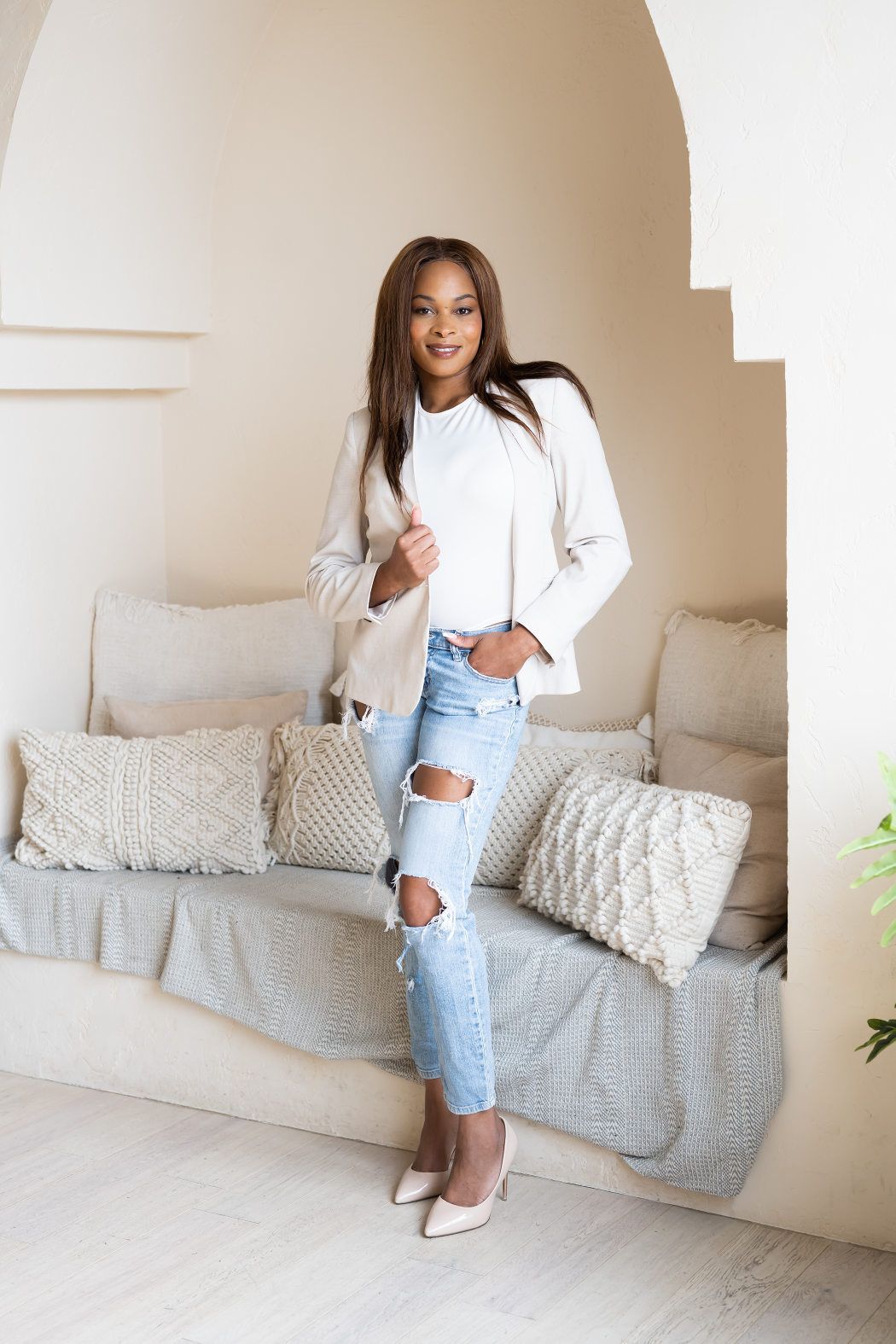 Youthful woman with a bright smile, wearing a white jacket and top, paired with torn blue jeans, casually resting hand in pocket
