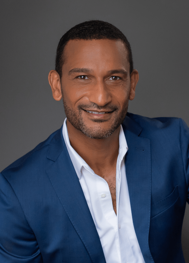 A professional headshot of a man wearing a navy suit and crisp white shirt