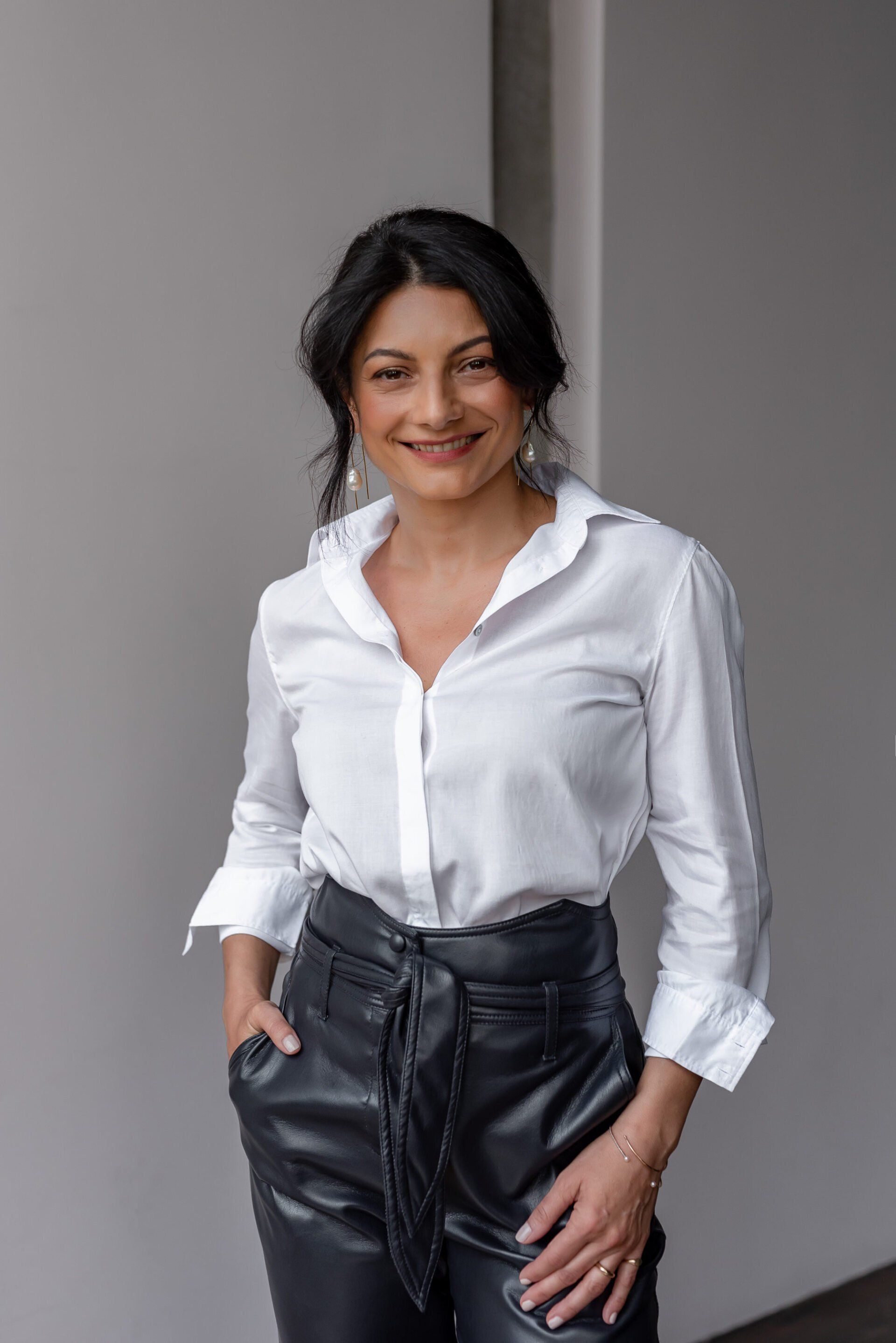 A female executive standing square to the camera with one hand relaxed at her side and the other resting in her pocket