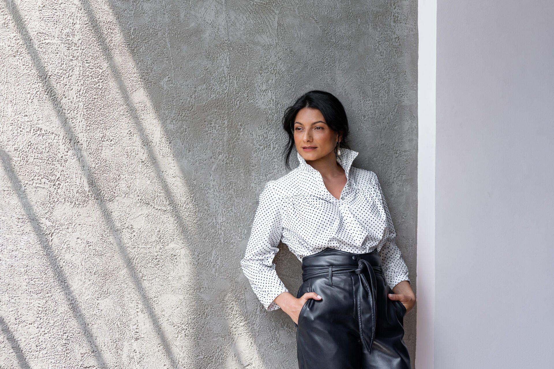 A woman in a white shirt and black pants is leaning against a wall.