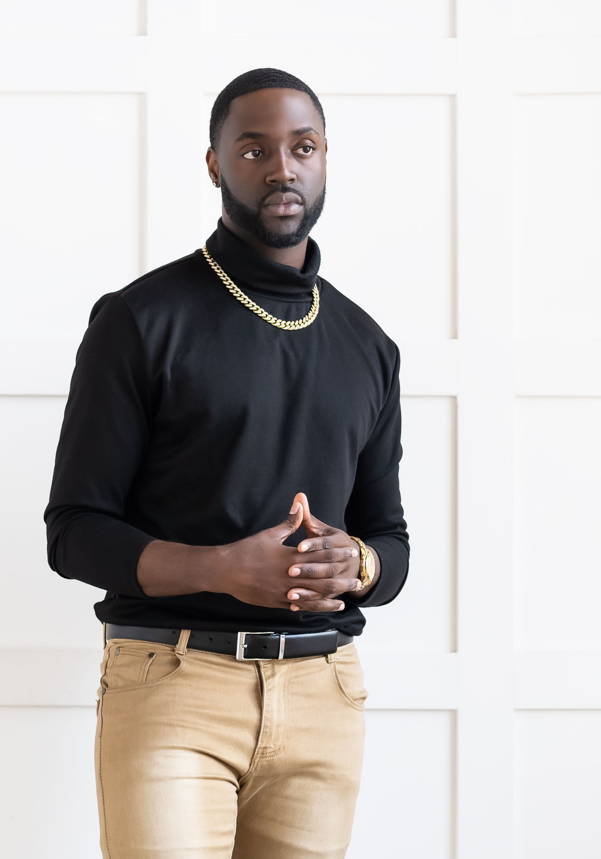 male wearing black turtle neck top with a gold necklace posing for a photo