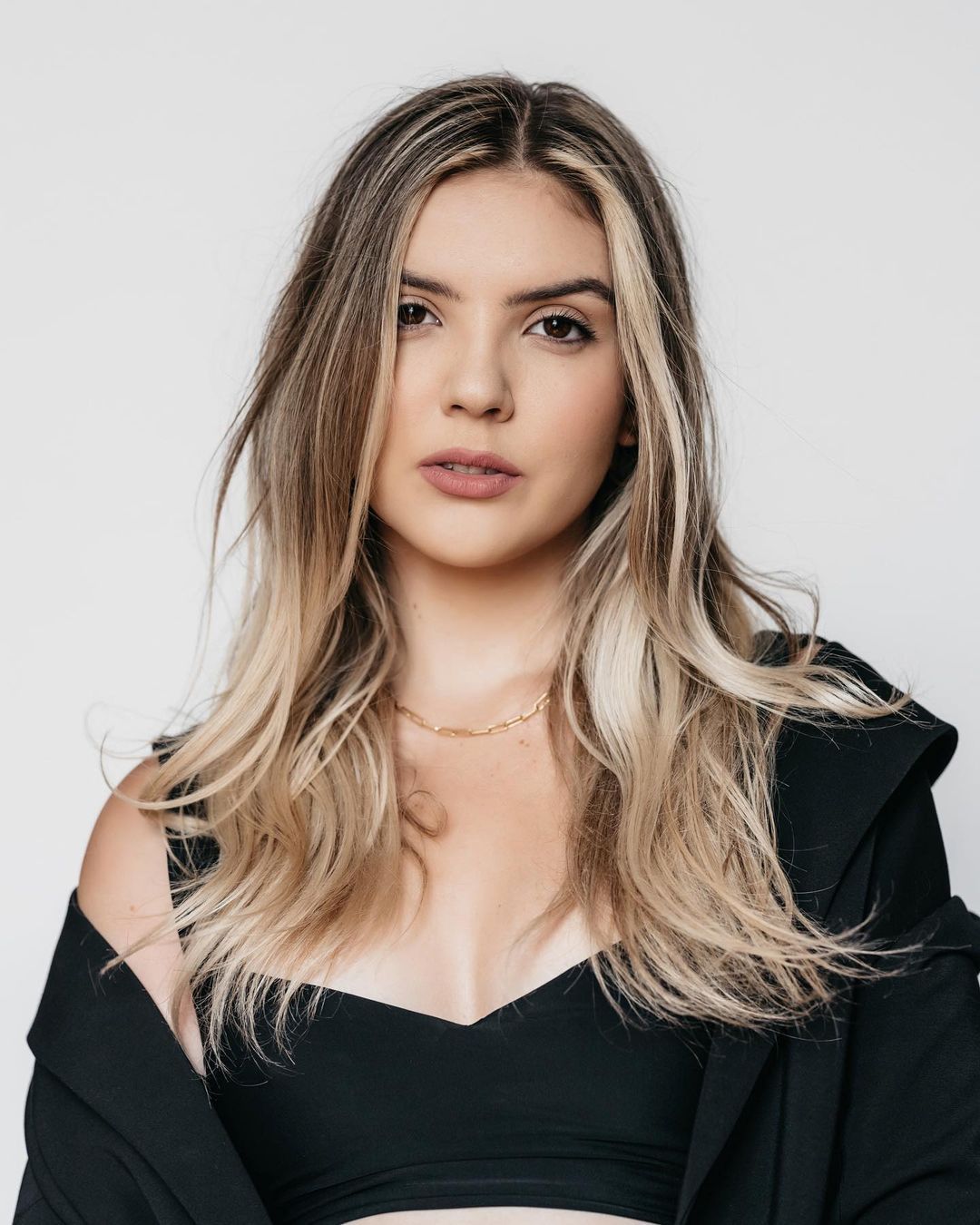 woman with long blonde hair wearing black top and blazer looking at the camera