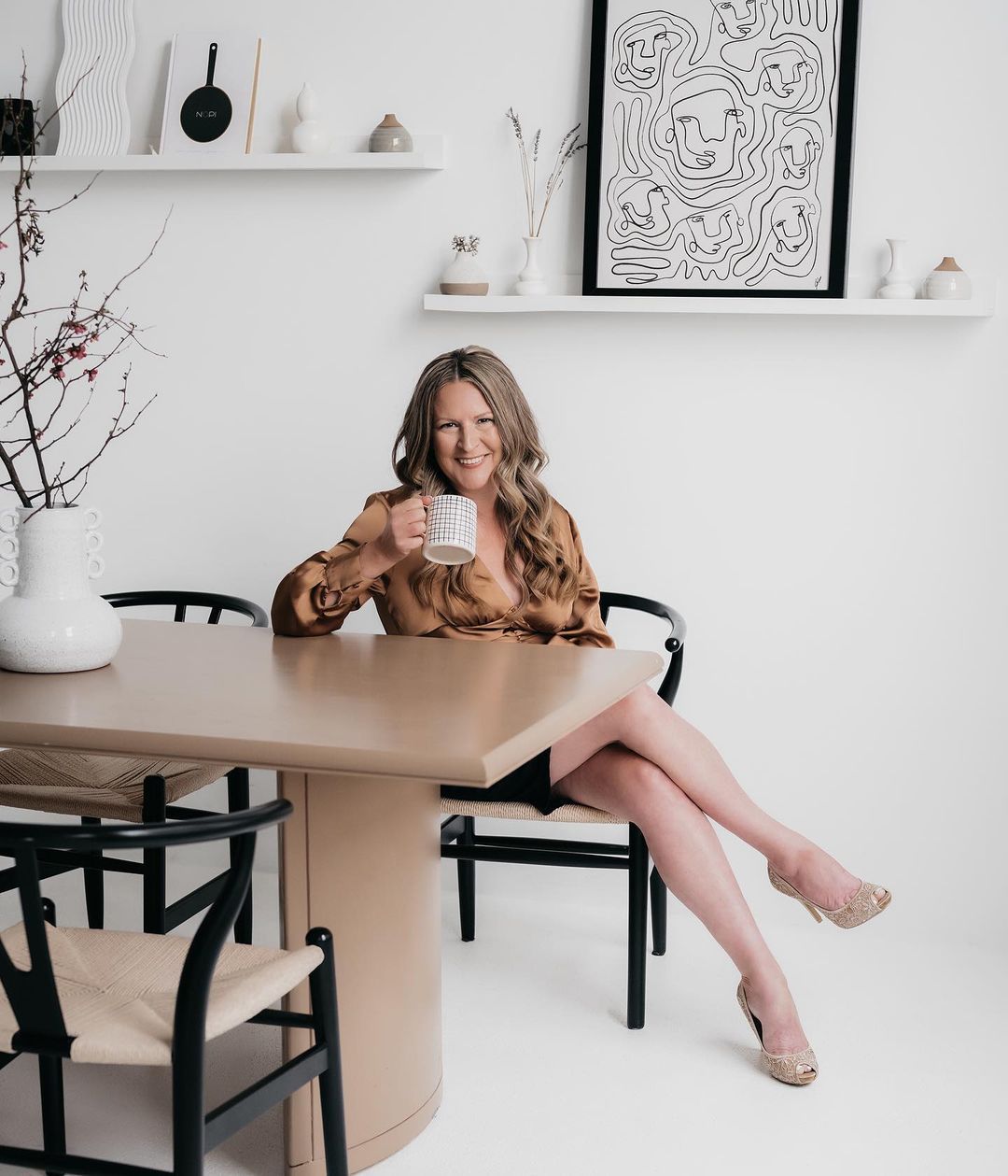 woman in a golden brown top sitting on a chair with a cup on her hand smiling at the camera