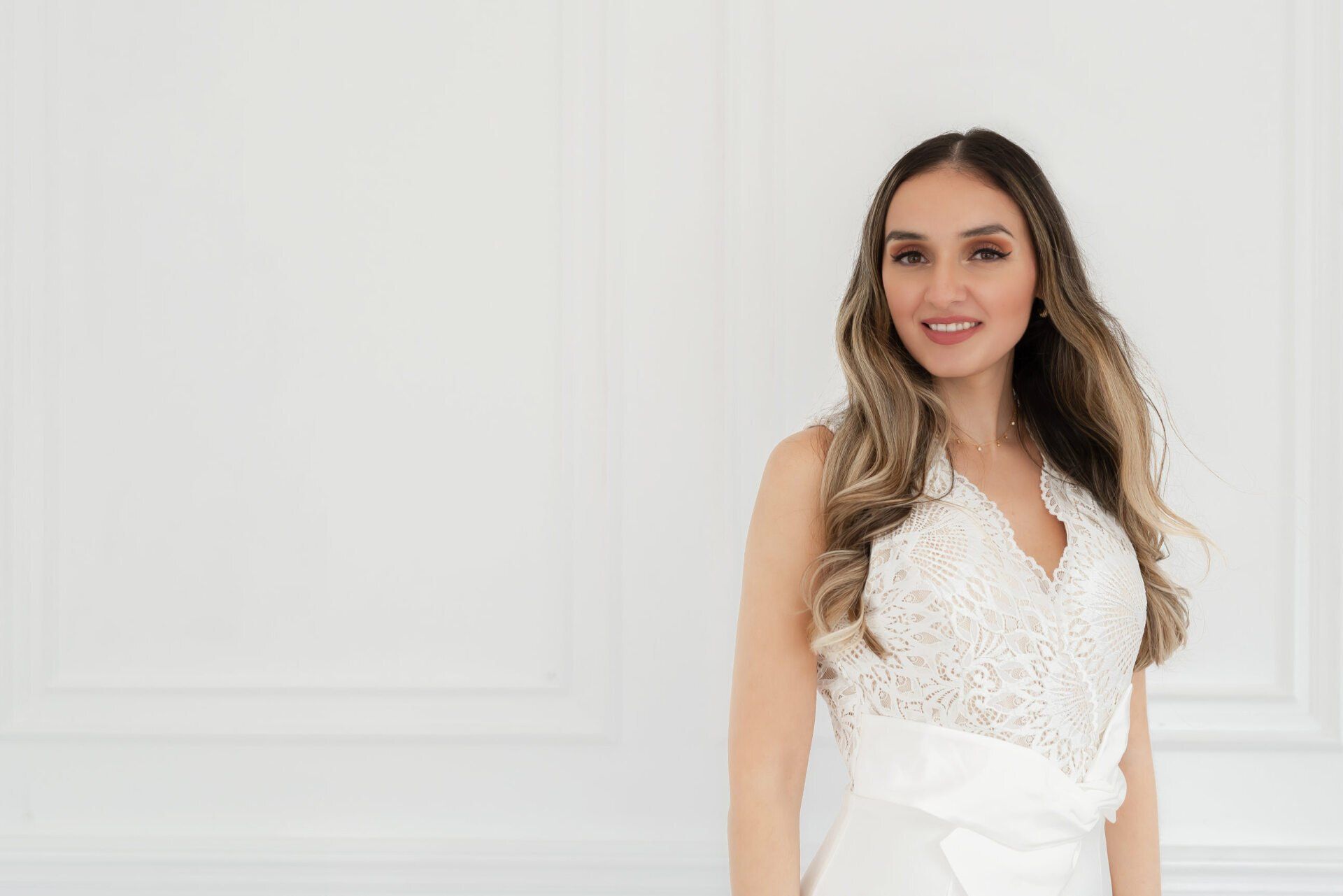 A confident woman dressed in white stands against an all-white wall in a headshot photo.