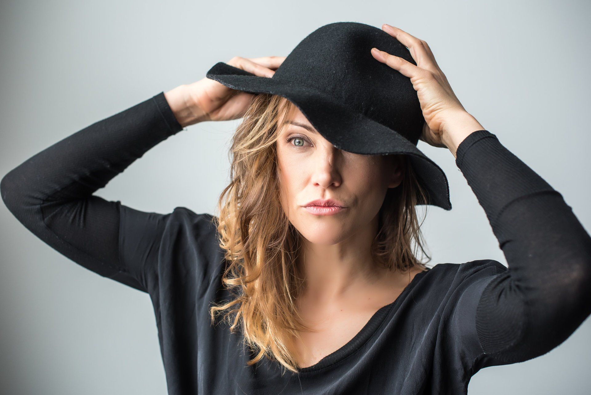 A woman wearing a black hat is covering her face with her hands.