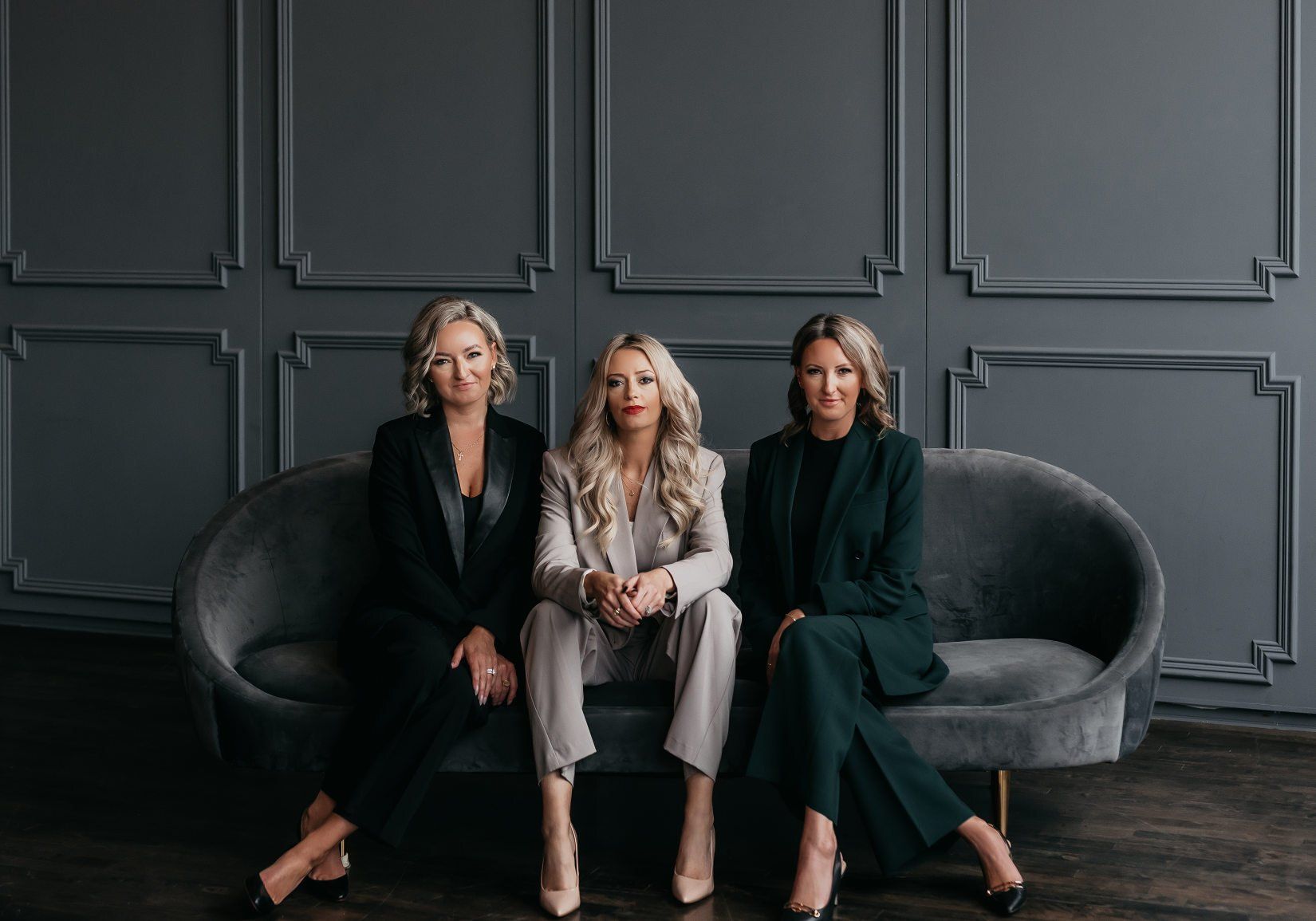 Three women in suits are sitting on a couch.