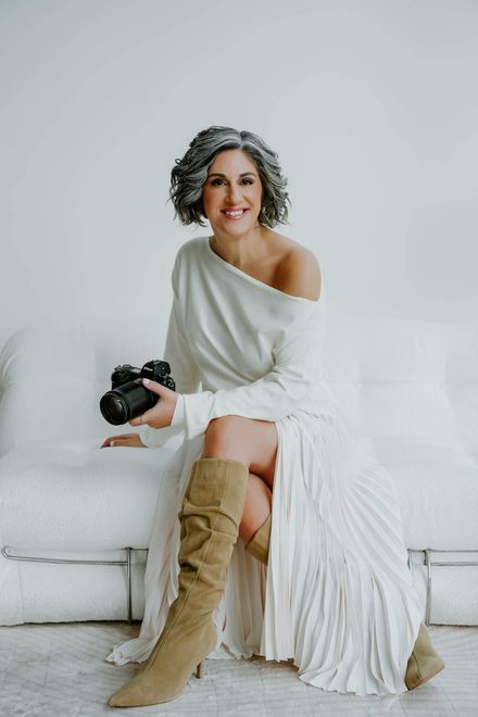 Stacey Naglie sitting on a white couch holding a camera.