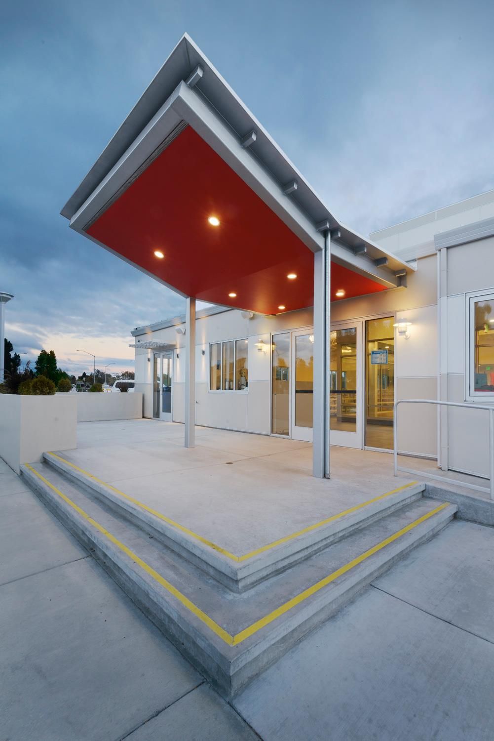 Modern house entrance with red canopy, yellow-edged steps, and glass doors at dusk