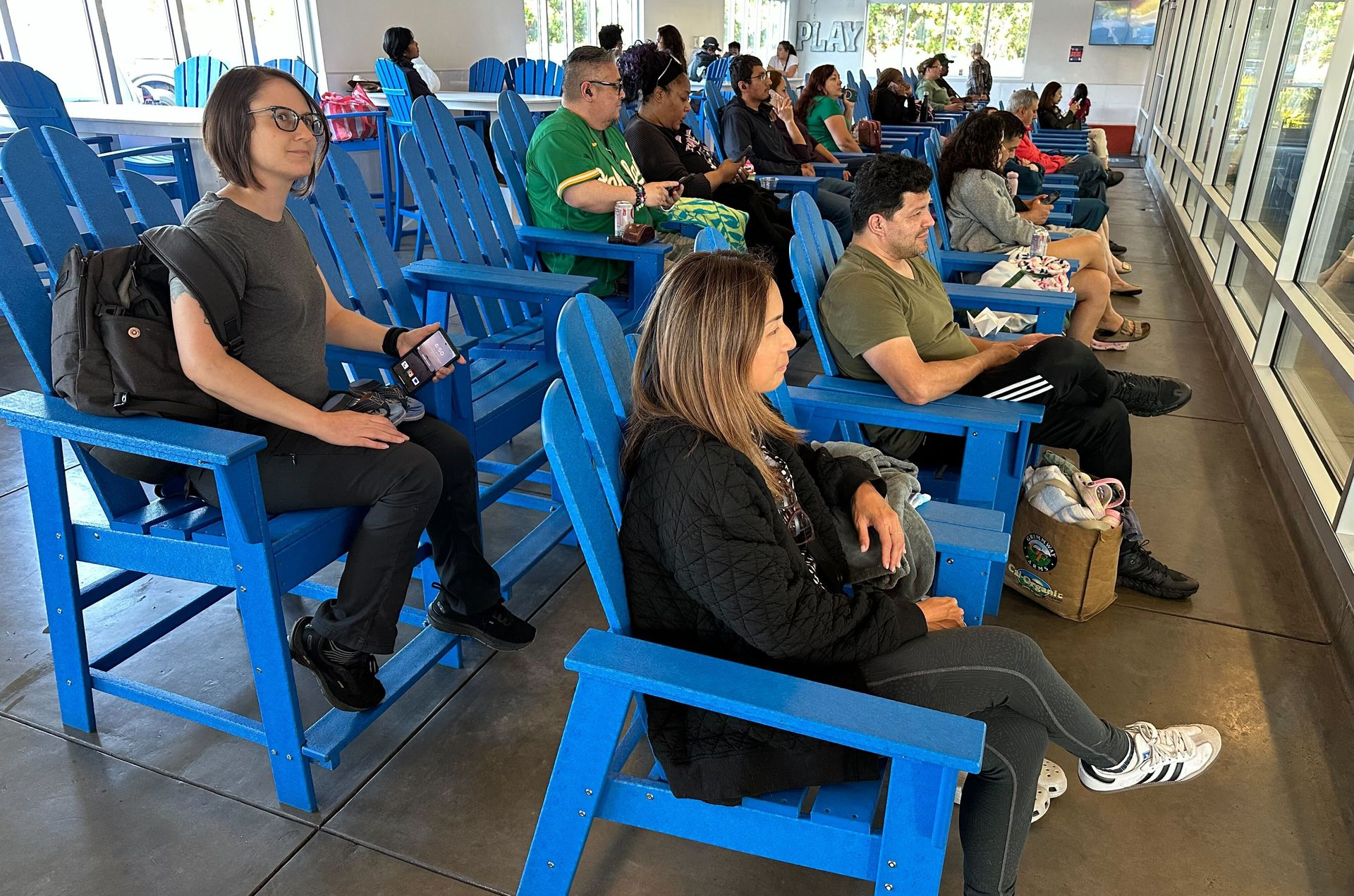People seated in blue stadium chairs watching an event indoors