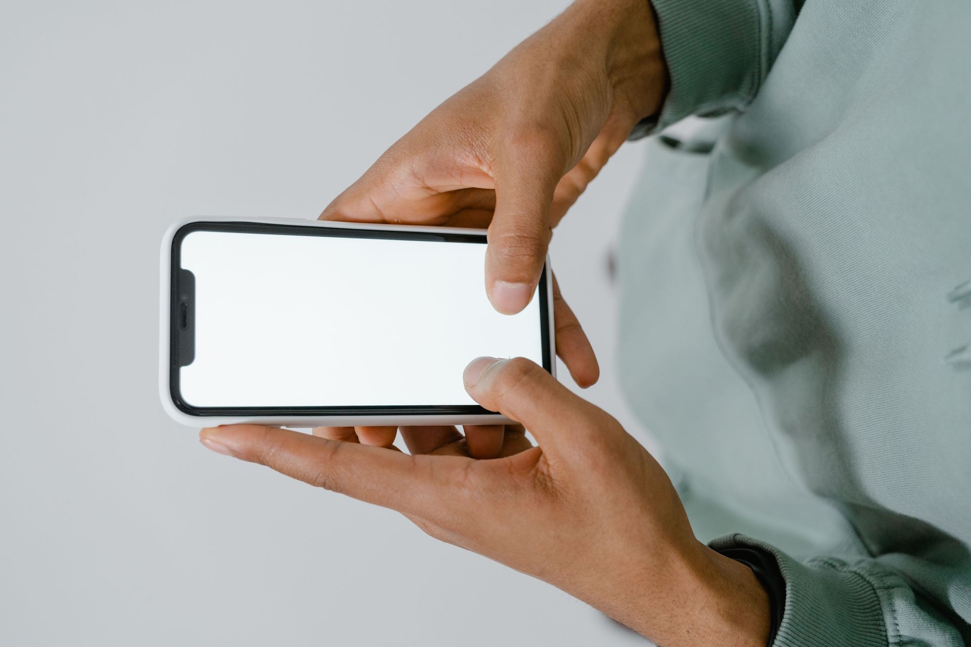 Hands holding a smartphone with a blank white screen in landscape orientation