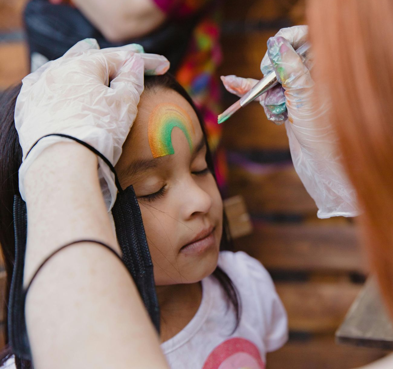 Adult painting a child’s face with colorful makeup at a festive event
