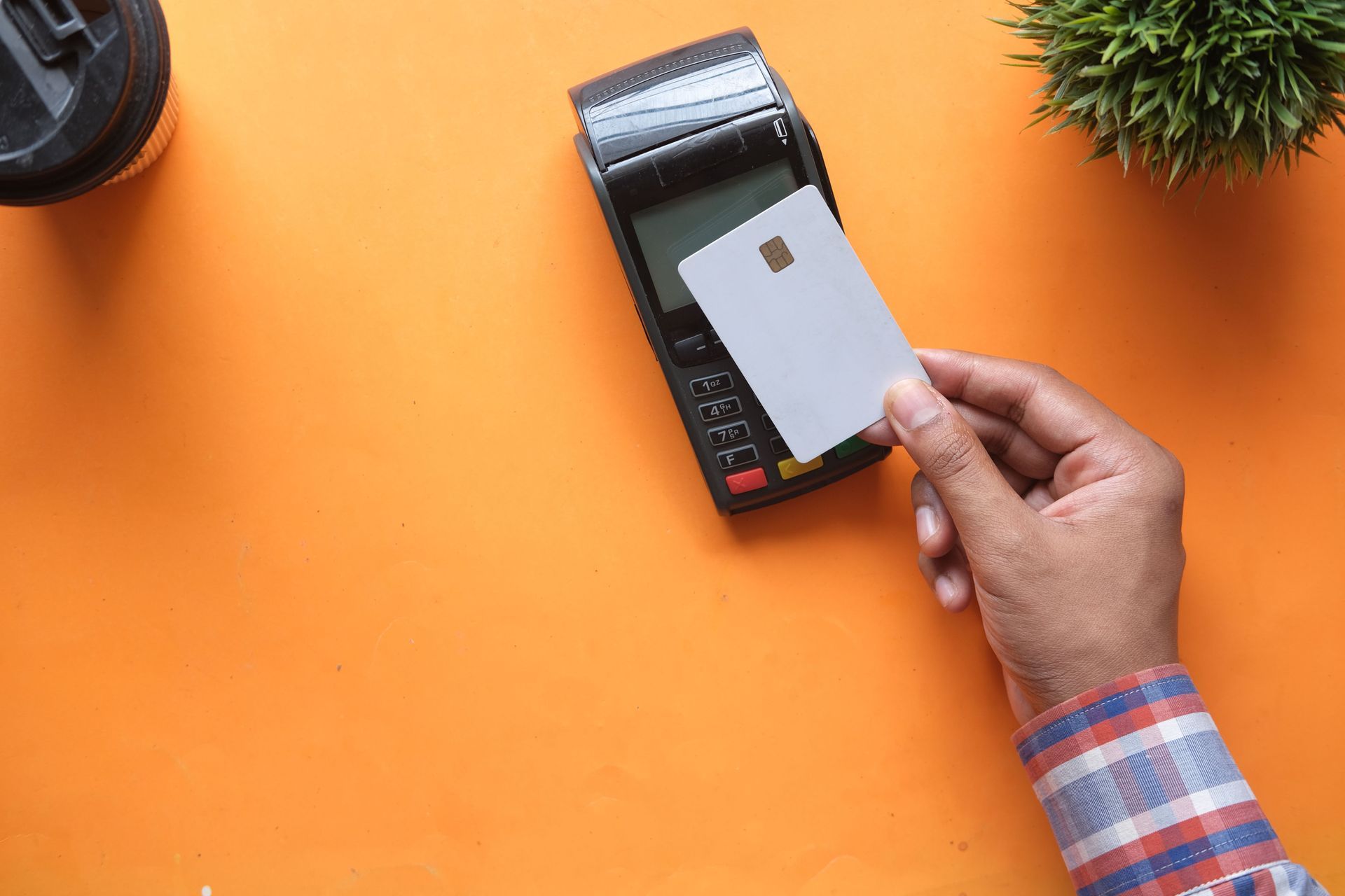 Hand holding a card over a payment terminal on an orange desk