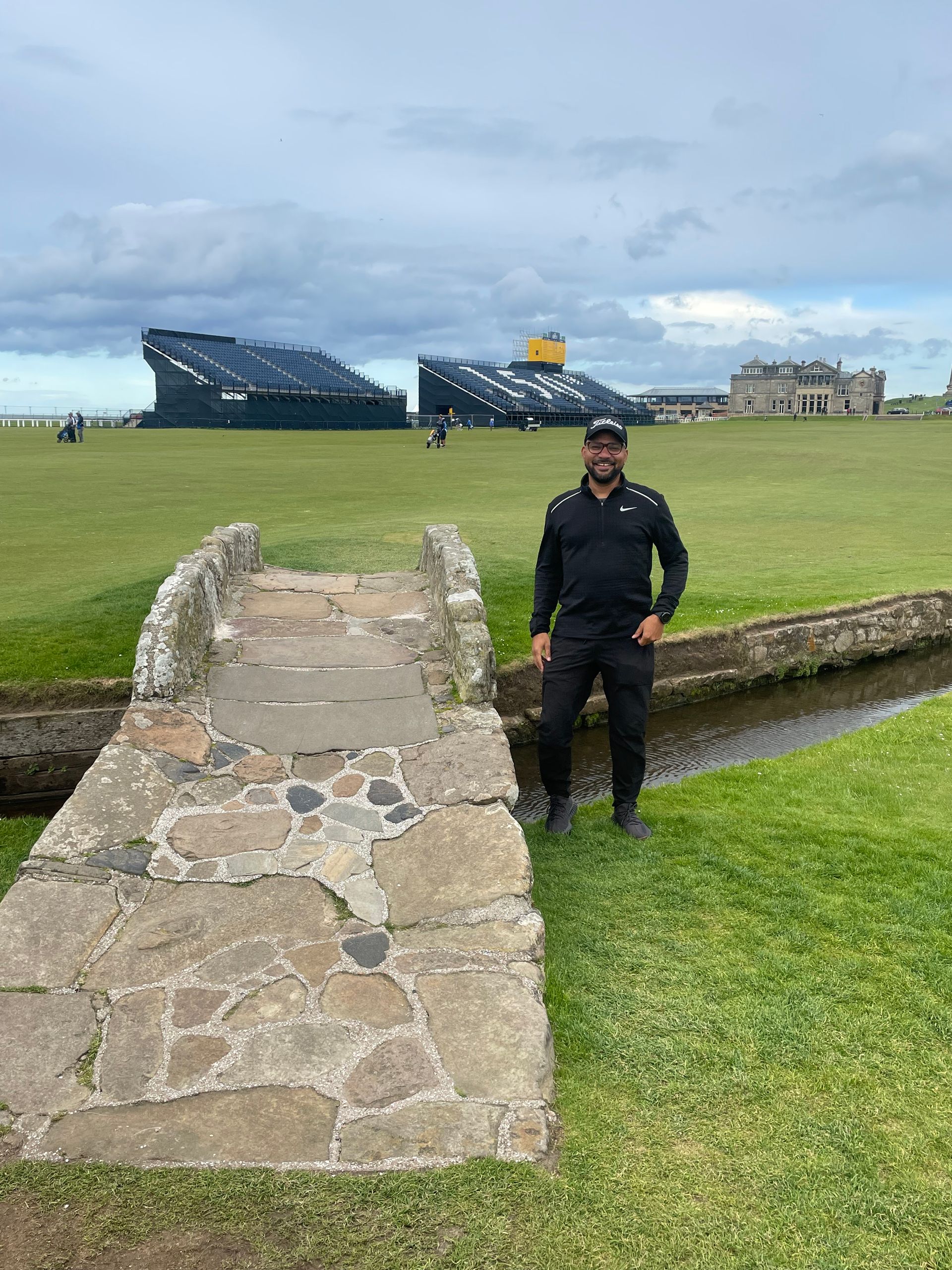 beau mitcham is standing next to a stone bridge on a golf course.