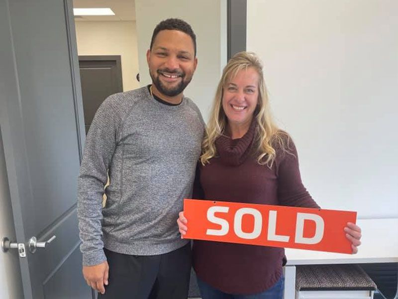 beau mitcham and a woman are holding a sold sign.