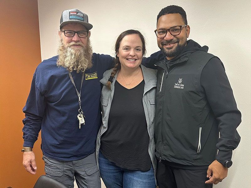 beau mitcham with a beard is standing next to a woman and a man with glasses.