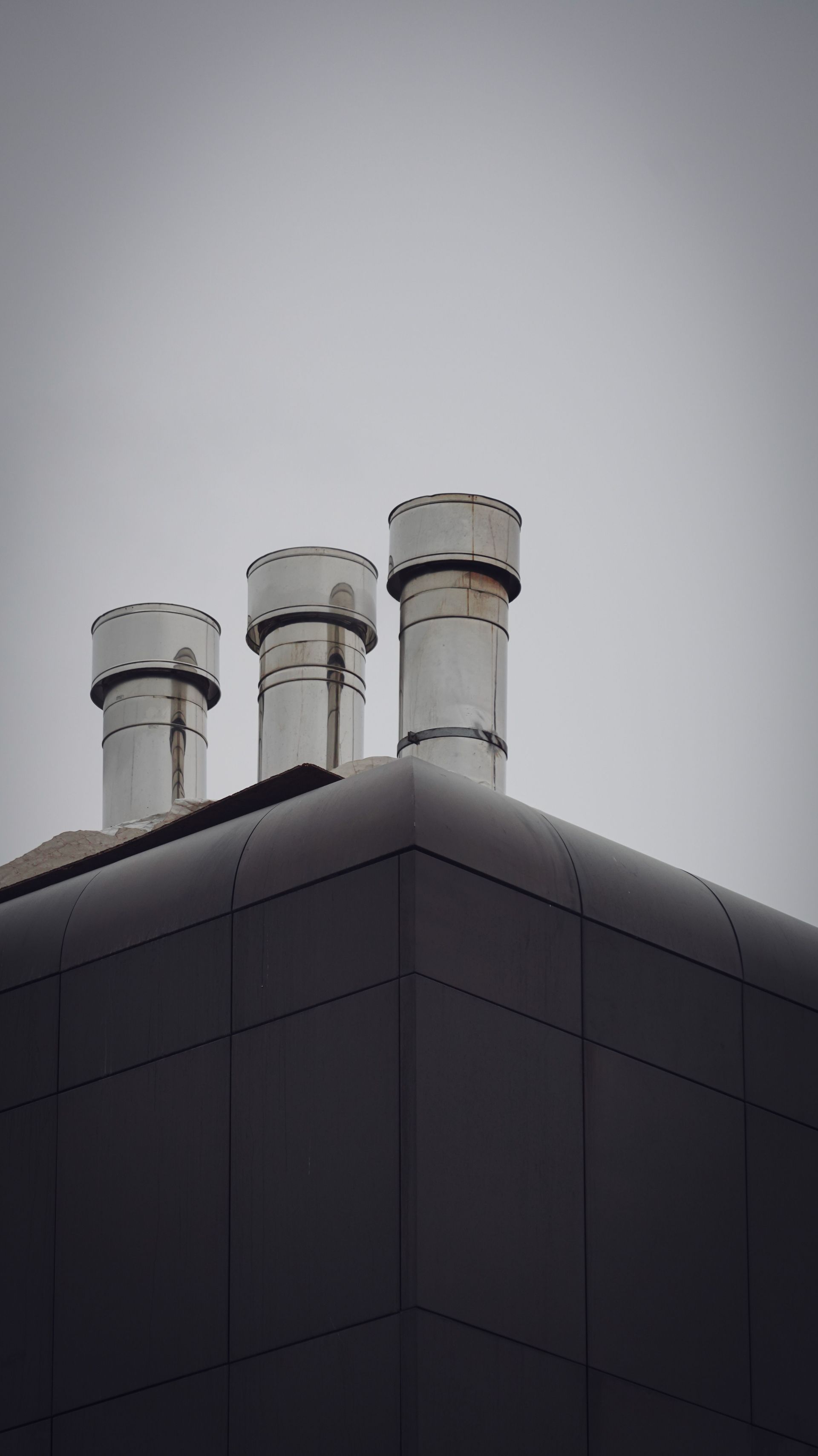 Three metal chimneys on a dark building rooftop against a gray sky