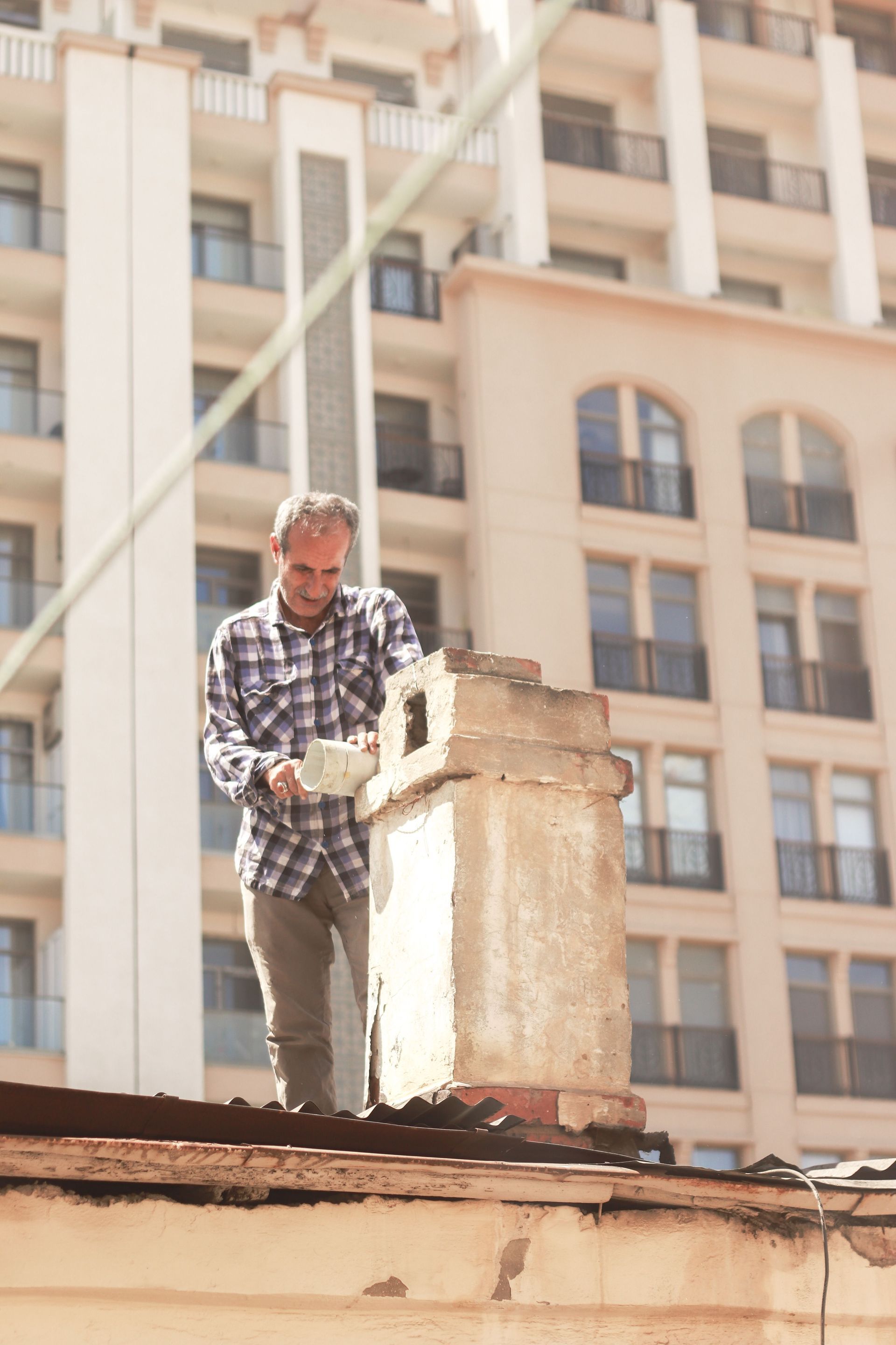 Man repairing a chimney on a rooftop in front of a tall apartment building
