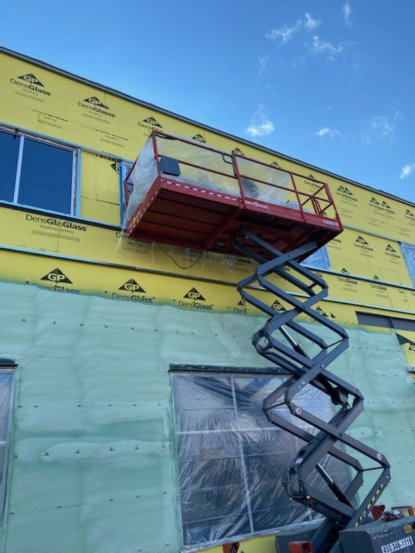Plateforme élévatrice à ciseaux rouge à côté d'un bâtiment en construction avec un ciel bleu.