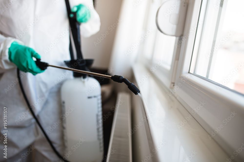 A man in a protective suit is spraying a window with a sprayer.