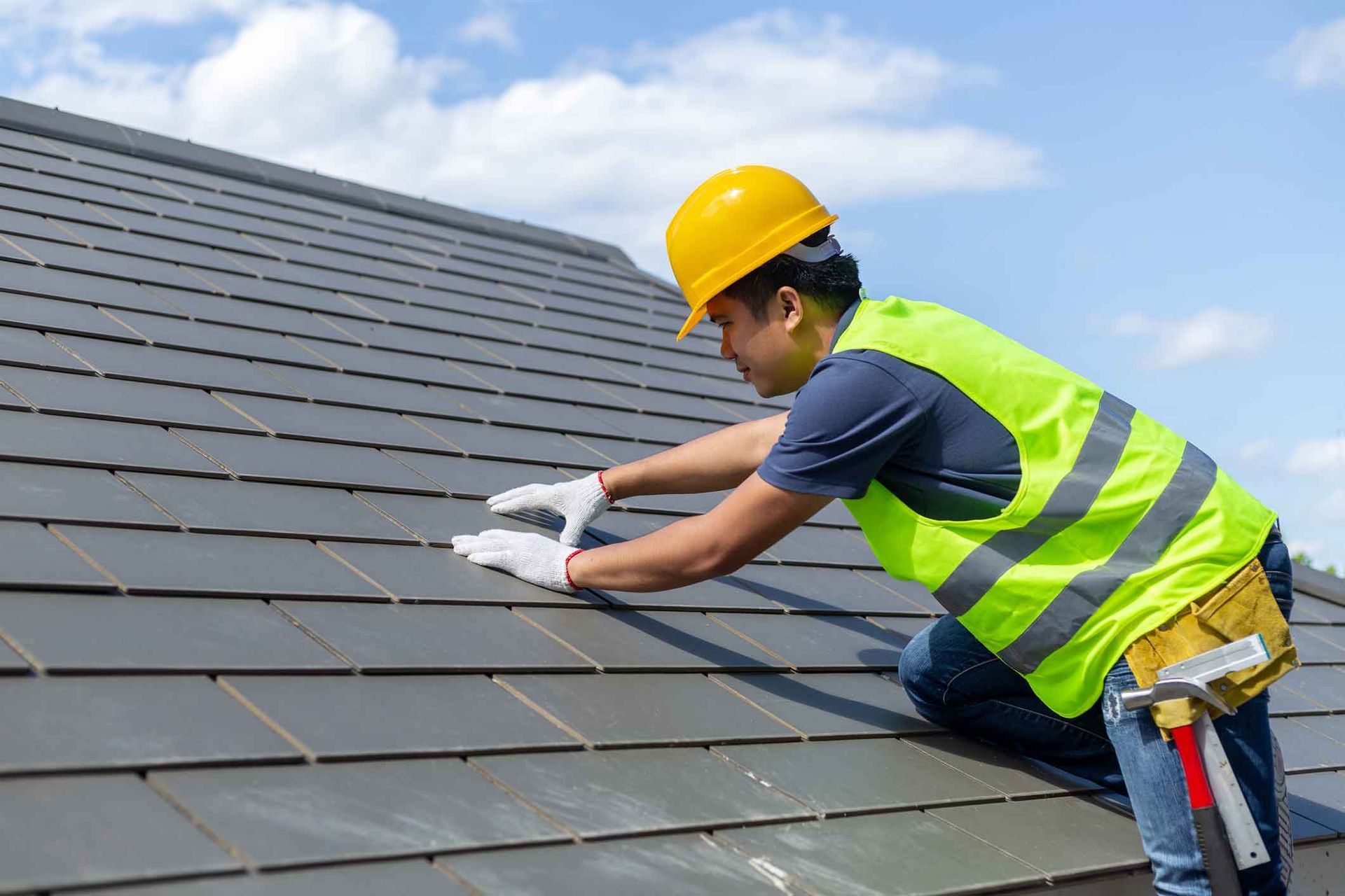 A man wearing a hard hat and safety vest is working on a roof.