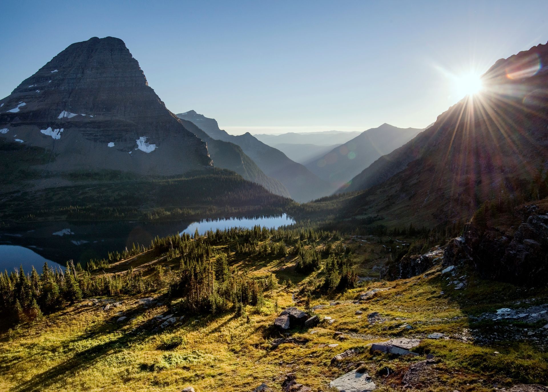 Sun setting over mountains, illuminating a lake and valley.