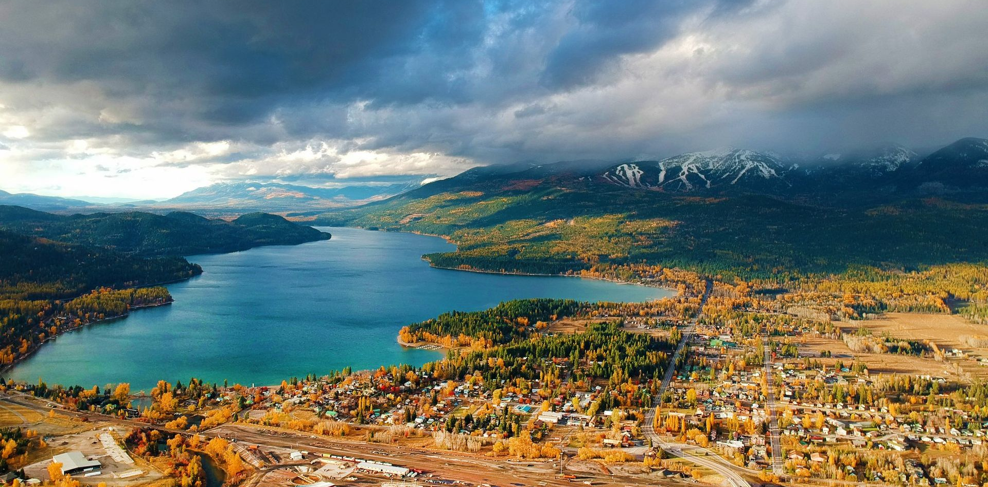 Aerial view of a lake surrounded by mountains and a town under a cloudy sky.
