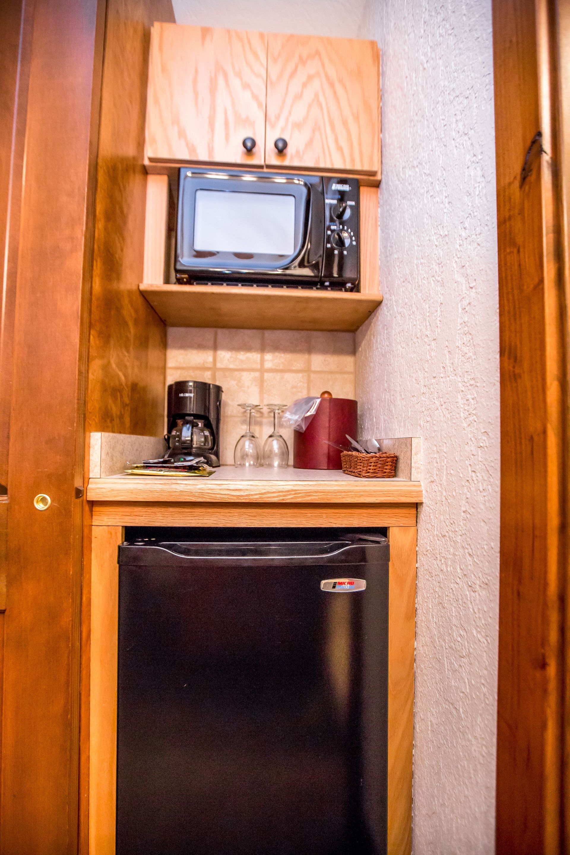 Mini-kitchenette with microwave, mini-fridge, coffee maker, and cabinets, built into a wooden alcove.