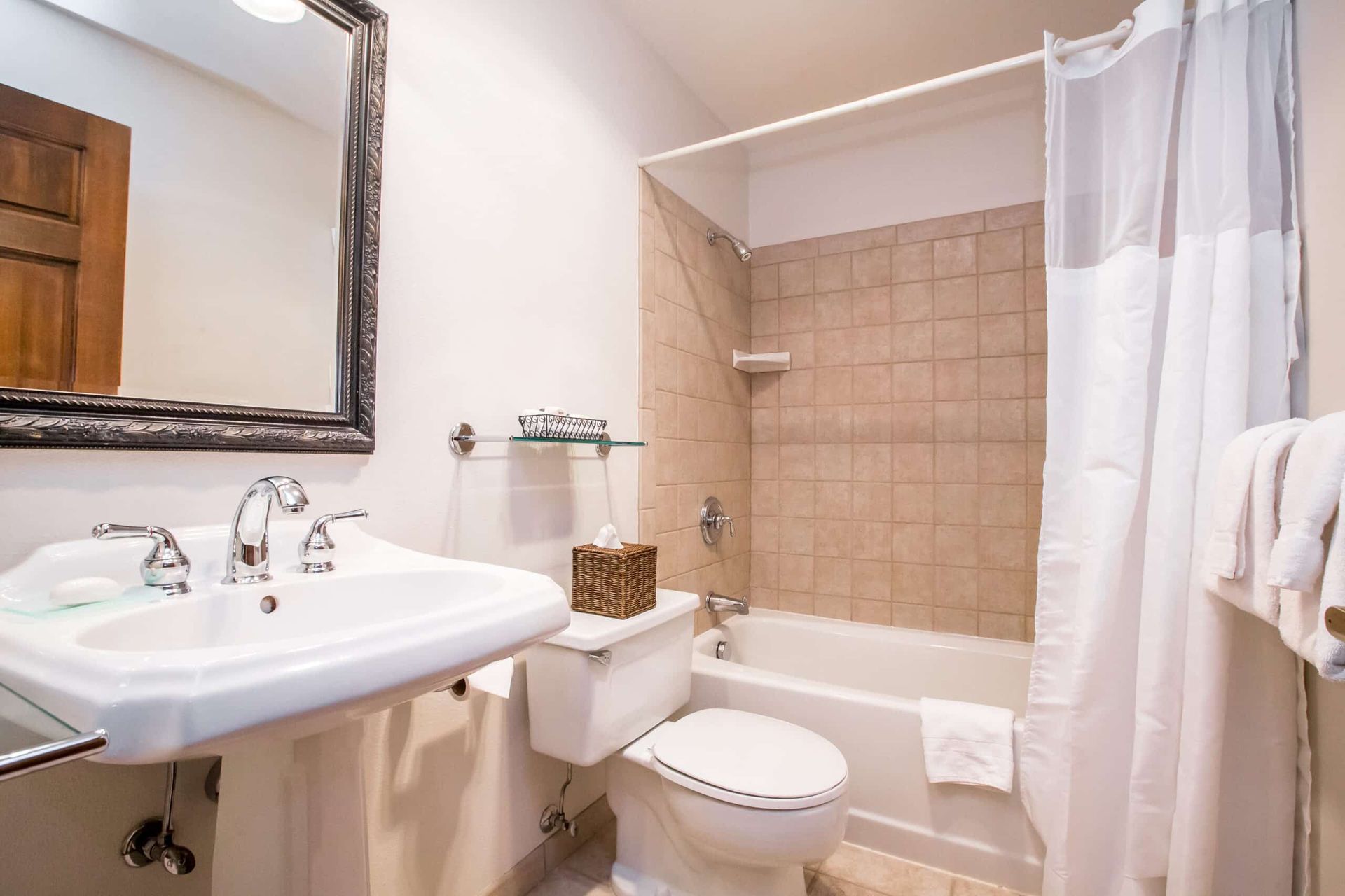 Bathroom with white sink and toilet, shower with beige tiled wall, mirror.