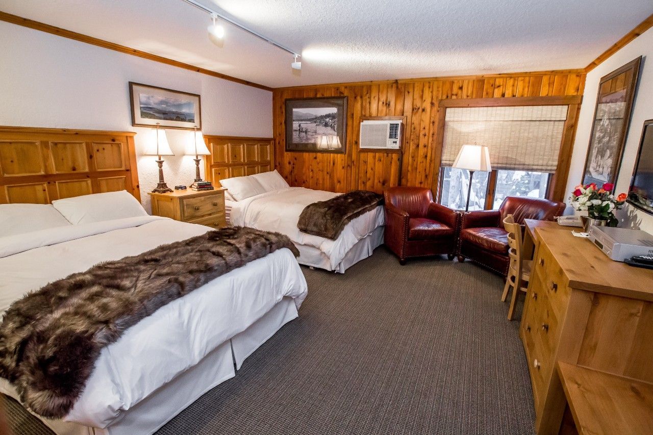 Hotel room with two beds, wood paneling, armchair, and a desk.