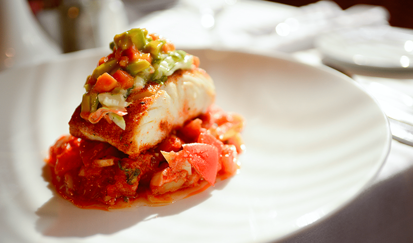 White fish fillet topped with avocado salsa, served on a bed of tomato sauce on a white plate.