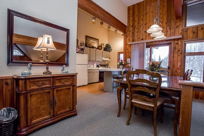 Dining room and kitchen with a wooden cabinet, large mirror, and dining table with chairs. Light walls, a window with a view, and recessed lighting.