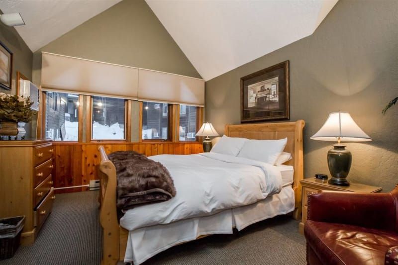 Bedroom with a bed, nightstands, red chair, and wooden paneling around a window looking out onto snow.