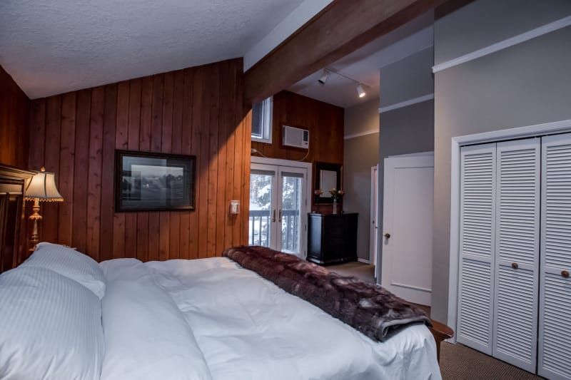 Bedroom with wood paneling, a large bed, and a doorway leading to another room. Includes a fur throw.