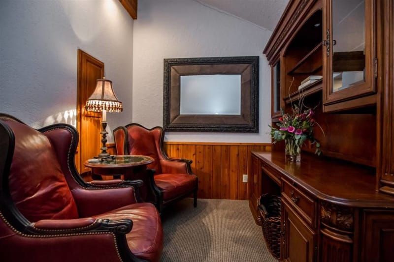 Cozy office nook with two red leather armchairs, a wooden desk, and a large mirror. The room has warm lighting and wood paneling.