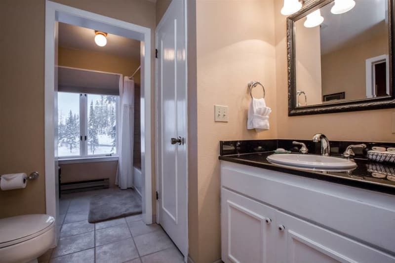 Bathroom with white vanity, black countertop, and a doorway leading to a window with an outdoor view. Beige walls and white trim.