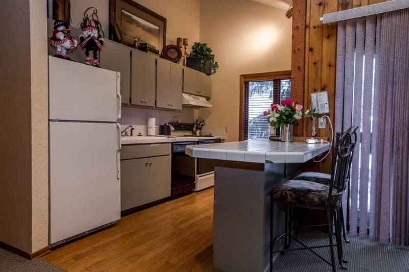 Kitchen with white appliances, grey cabinets, and a breakfast bar. Wooden accents and natural light.