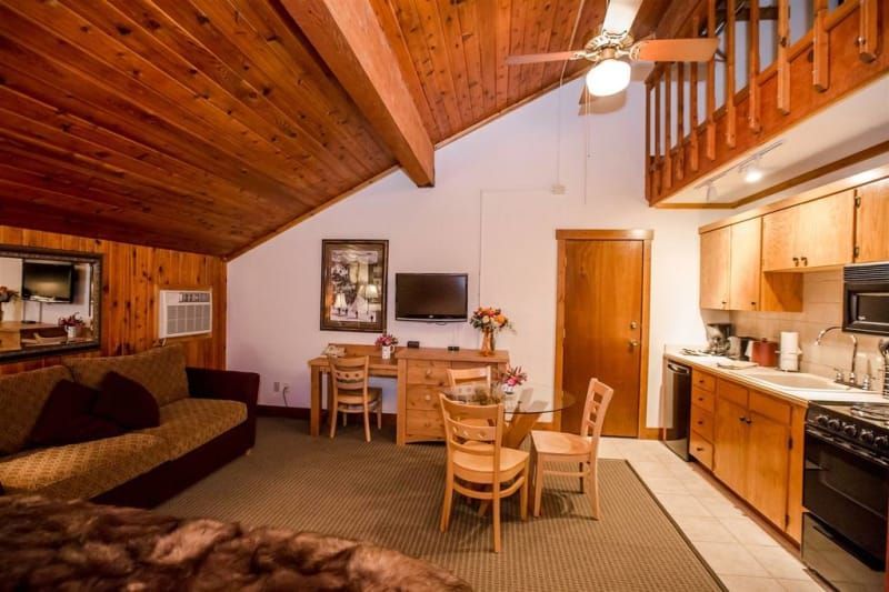 A cozy cabin interior with wood paneling, a small kitchen, living area with a sofa, and a loft.