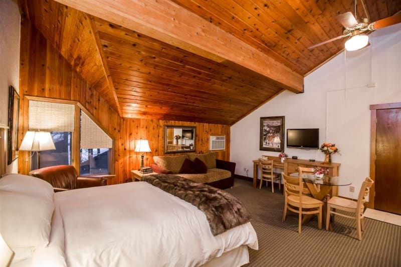 A hotel room with wood paneling and a sloping ceiling. It contains a bed, seating area, desk, and television.