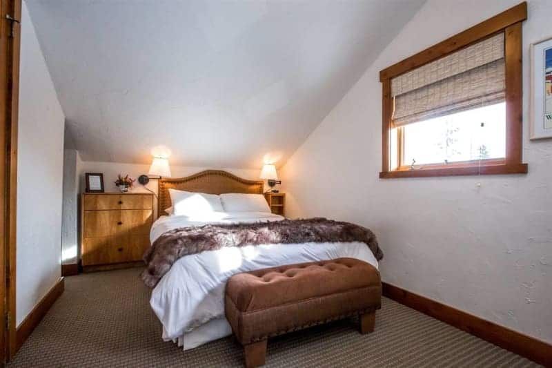 Bedroom with a double bed, brown ottoman, wooden dresser and window with blind.
