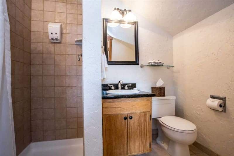 Small bathroom with a shower, toilet, and sink. The shower has tile walls, and the sink has a wooden cabinet.